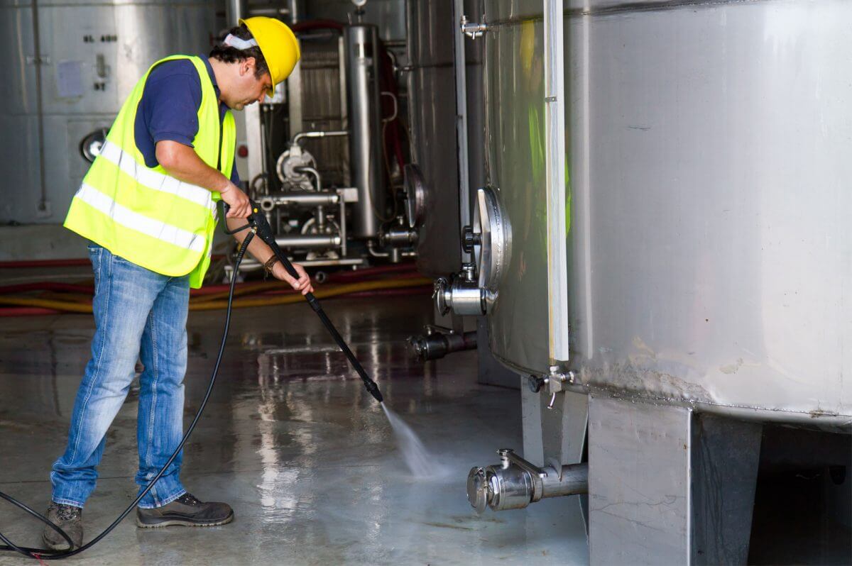 Operario utilizando hidrolavadora industrial Alfa 2 para limpiar tanque de alimentos